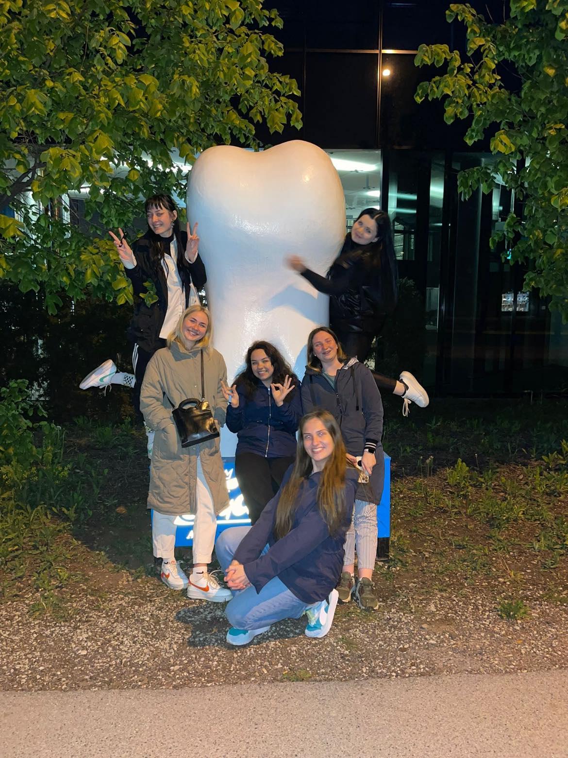 Stomatoloģijas studentes pozē pie liela zoba statujas