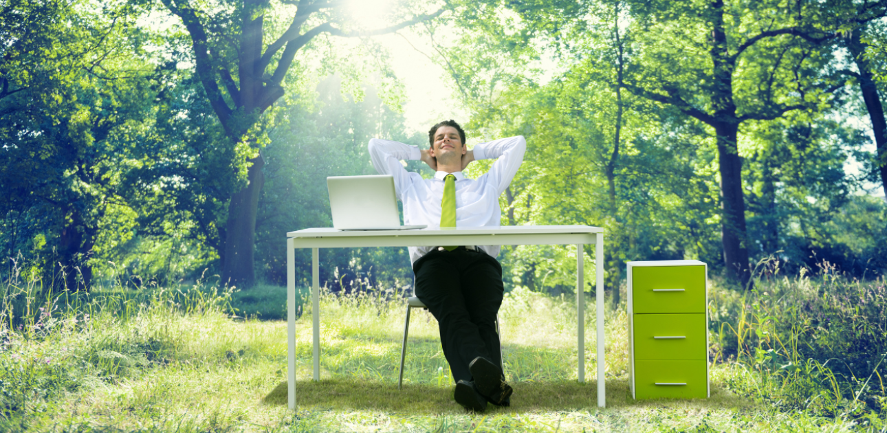 Vīrietis dabā ar zaļiem kokiem sēž pie biroja galda