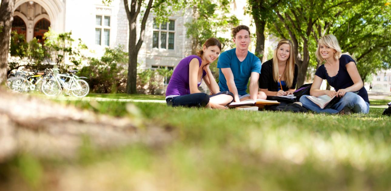 Četri studenti sēž zālītē pie universitātes