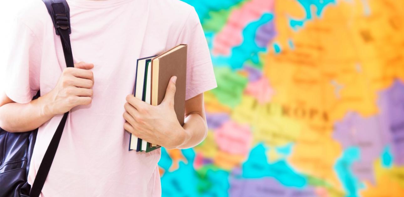 Students ar mugursomu un grāmatām stāv pie Eiropas kartes