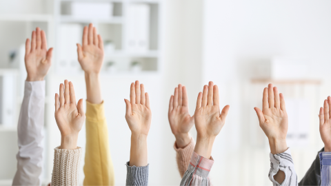 vairāku cilvēku rokas paceltas gaisā, fonā biroja telpas